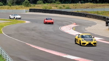 Varios Porsches, incluyendo un Cayman amarillo en primer plano, compitiendo en una curva de una pista de carreras.