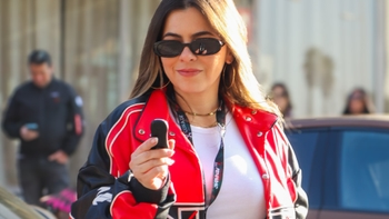 Mujer con chaqueta roja y gafas de sol sosteniendo el llavero de un coche en un evento automovilístico.