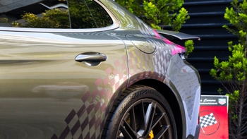 Detalle lateral trasero de un Porsche 911 Carrera GTS con vinilo cuadriculado rosa sobre la carrocería, alerón desplegado y rueda visible.