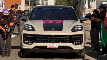 Porsche SUV con vinilo P7 en el capó, flanqueado por fotógrafos y asistentes en la salida de un evento automovilístico.