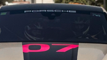 Detalle del capó con vinilo rosa "P7" y parabrisas con el logo Porsche; se distinguen los cascos de los pilotos en el interior.