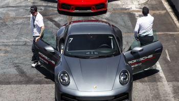 Vista aérea frontal de un Porsche 911 gris con ambas puertas abiertas en el pit lane, con asistentes alrededor del vehículo.