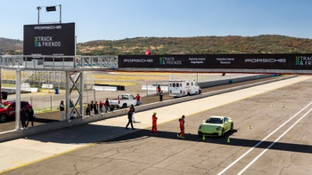 Porsche 911 color lima detenido en el pit lane, con personal del circuito y una ambulancia al fondo.