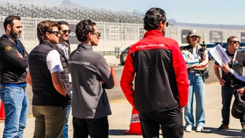 Grupo de participantes y personal con chaquetas Porsche recibiendo instrucciones en el pit lane antes de salir a la pista.