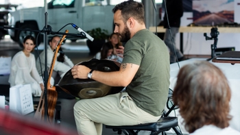 Hombre tocando un handpan en un evento con público, con una guitarra y otros elementos en el fondo.