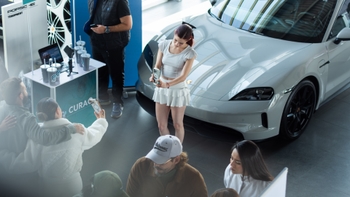Mujer posando frente a un Porsche Taycan blanco para una foto, rodeada de personas y elementos promocionales.