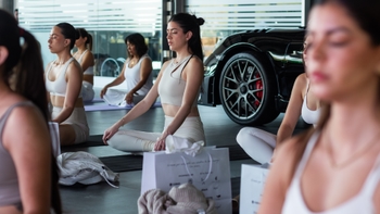 Mujeres meditando junto a un Porsche negro en un evento, combinando bienestar y estilo de vida automotriz.