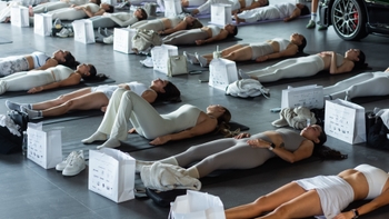 Grupo de mujeres practicando yoga en un espacio con un Porsche al fondo y bolsas de regalo con logos de marca.