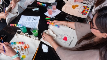 Manos de participantes pintando bolsos de tela con el logo Porsche durante una actividad creativa del evento.