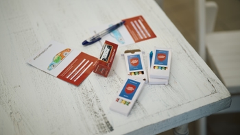 Artículos de Porsche sobre una mesa blanca: hojas para colorear coches, cajas de crayones con el lema 'Juntos acelerando sueños' y otros artículos promocionales.