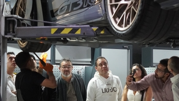 Un grupo de personas observa de cerca un Porsche 911 GT3 RS elevado en un sistema de mantenimiento dentro de un taller.