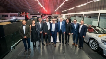Grupo de personas vestidas formalmente posando junto a un Porsche en un evento de Porsche.