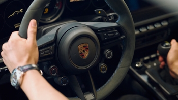 Manos de una persona sujetando el volante alcantara y la palanca de cambios de un Porsche 911 GT3, con reloj en la muñeca.