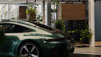 Vista trasera de un Porsche 911 Carrera verde estacionado en el showroom, destacando el diseño del auto y la decoración con plantas.