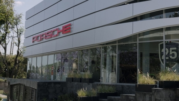 Fachada frontal de un Porsche Centre Santa Fe con el logotipo rojo, amplios ventanales, plantas decorativas y un árbol en el exterior.