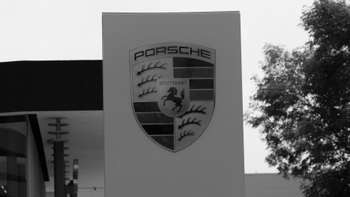 Letrero exterior en blanco y negro con el emblemático escudo de Porsche, mostrando el logo de la marca, el caballo rampante y la palabra 'STUTTGART'.