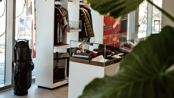 Interior de una tienda Porsche con ropa, accesorios y un carrito de golf, enfocándose en la mercancía de la marca.