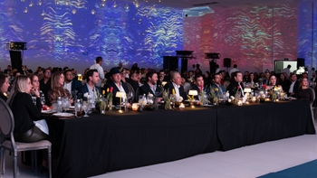 Invitados sentados en mesas decoradas, observando la presentación y las proyecciones lumínicas en una gala.