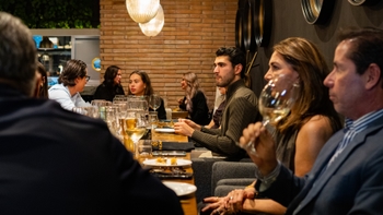 Invitados sentados en una mesa larga durante la cena de gala, conversando y observando la presentación.