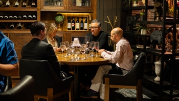 Invitados conversando alrededor de una mesa con copas y botellas durante una cena privada en el restaurante.
