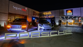 Letrero iluminado "Porsche" y dos coches estacionados frente a los restaurantes NOMA y Taco Urbano durante un evento nocturno.