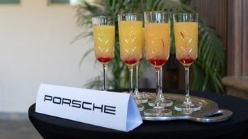 Cócteles amarillos en copas altas sobre una bandeja con el logo de Porsche, ambiente de evento.