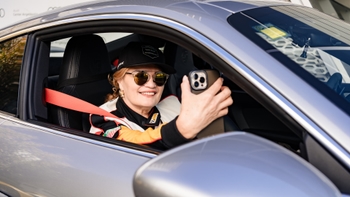 Mujer sonriente tomándose un selfie dentro de un auto Porsche