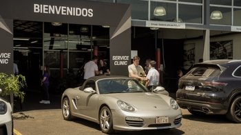 Exterior de una Porsche Service Clinic con un Porsche Boxster plateado estacionado y clientes siendo recibidos.