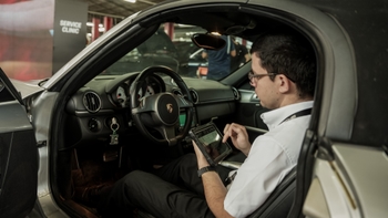 Mecánico de Porsche revisando el sistema de un auto con una tablet en el interior de un taller de servicio.