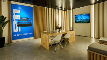 Interior de tienda de concesionario Porsche con exhibición de ropa, accesorios y un auto visible al fondo.