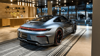 Porsche 911 gris de la parte trasera en un concesionario moderno con alfombra de diseño y detalles lujosos.