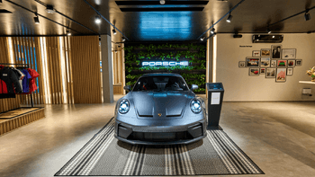 Porsche gris exhibido en un concesionario con paredes de madera, un jardín vertical y fotografías vintage de la marca en la pared.