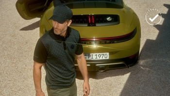 Hombre con estilo usando ropa Porsche Design parado frente a un Porsche verde con la puerta abierta, promocionando un estilo de vida sofisticado.