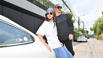 Pareja con estilo posando junto a un Porsche clásico blanco en una calle soleada, mostrando un estilo de vida moderno y elegante.