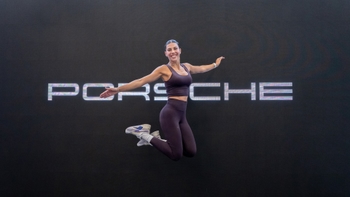Mujer saltando frente a valla de Porsche