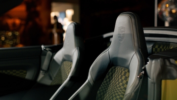 Primer plano de los asientos deportivos de un Porsche 911 descapotable; reposacabezas con el escudo Porsche grabado y tela interior con patrón a cuadros.