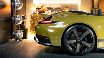 Primer plano del borde trasero y emblema 'Porsche 911 Turbo S' con la tira de luz roja encendida, reflejos y acabado brillante del vehículo.