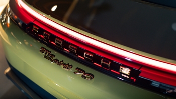 Primer plano del borde trasero y emblema 'Porsche 911 Turbo S' con la tira de luz roja encendida, reflejos y acabado brillante del vehículo.