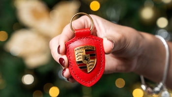 Llavero de cuero rojo con el escudo de Porsche, sostenido en la mano frente a un árbol de Navidad decorado.