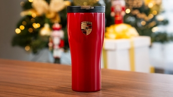 Termo rojo Porsche con el escudo de la marca, sobre una mesa de madera y un árbol de Navidad de fondo.